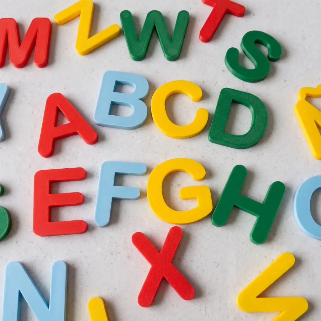 Letras imantadas de colores impresas en 3D, desparramadas sobre fondo de piedra clara
