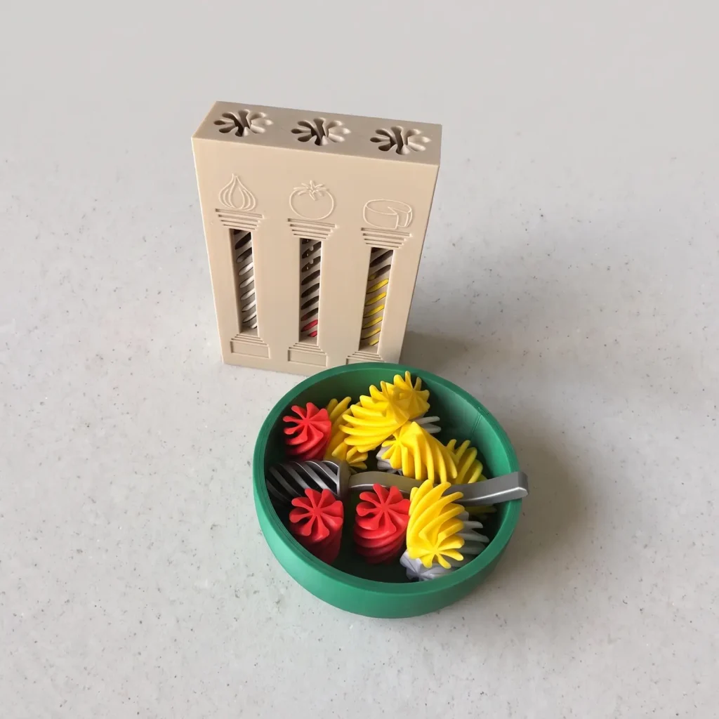 Caja de pasta beige con tres columnas ilustradas con ajo, tomate y queso, y un bowl verde con fideos espiralados de colores