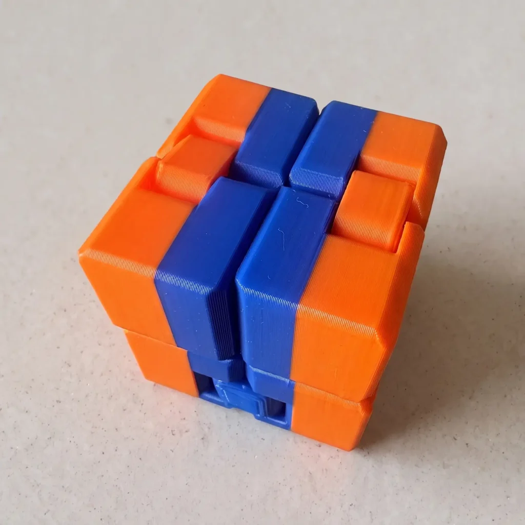 Cubo fidget impreso en 3D en naranja y azul, cerrado, sobre fondo de piedra clara
