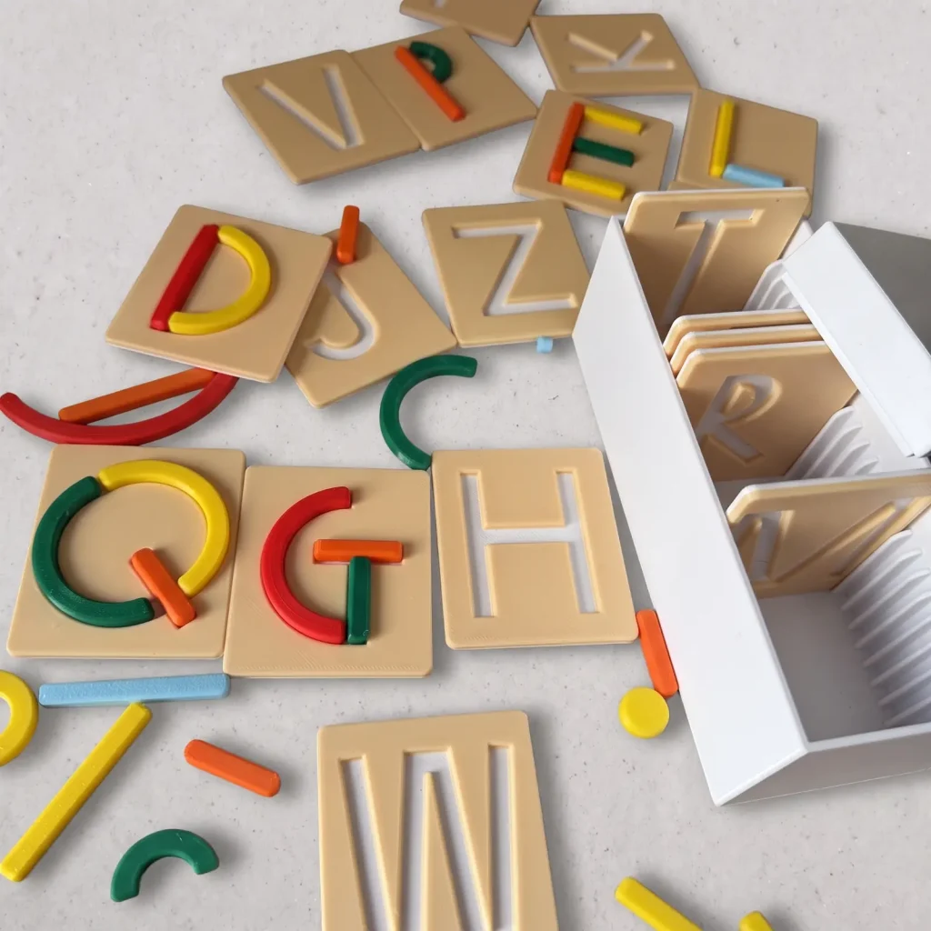 Tarjetas beige con letras en bajorrelieve completadas con trazos de colores impresos en 3D, junto a su caja