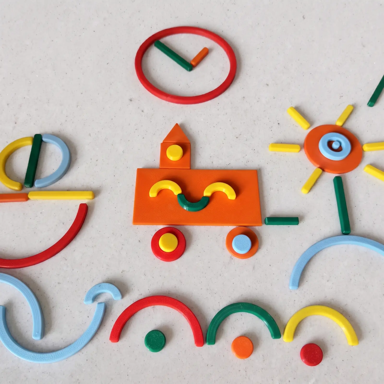 Piezas de colores impresas en 3D formando un tren, un reloj y un sol