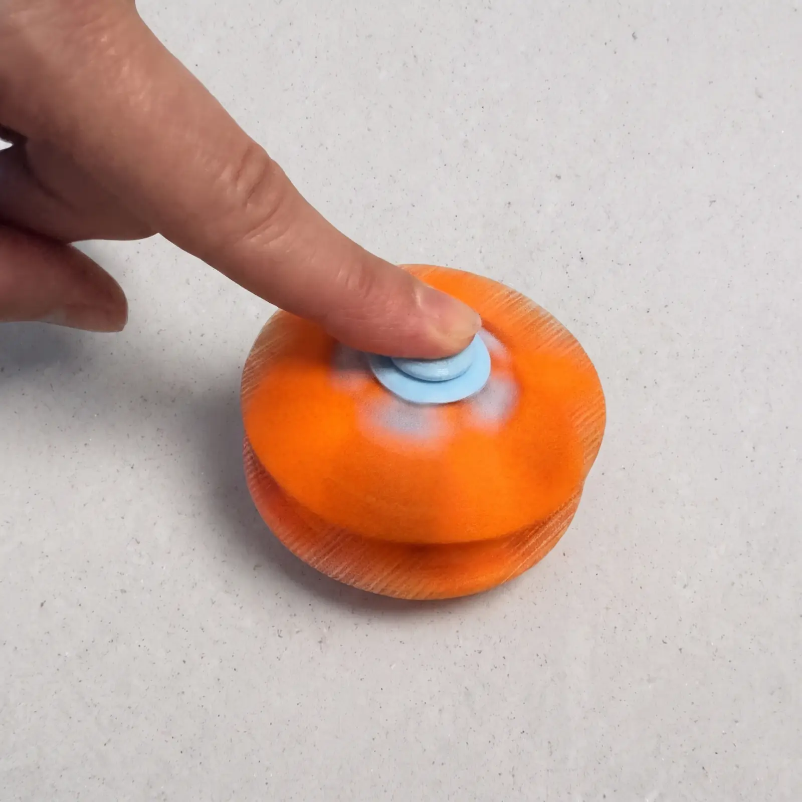 Dedo haciendo girar el trompo esfera naranja y celeste abierto como disco